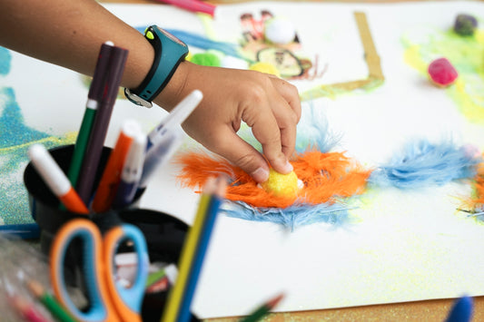 Child's hand creating art with colorful feathers and markers.